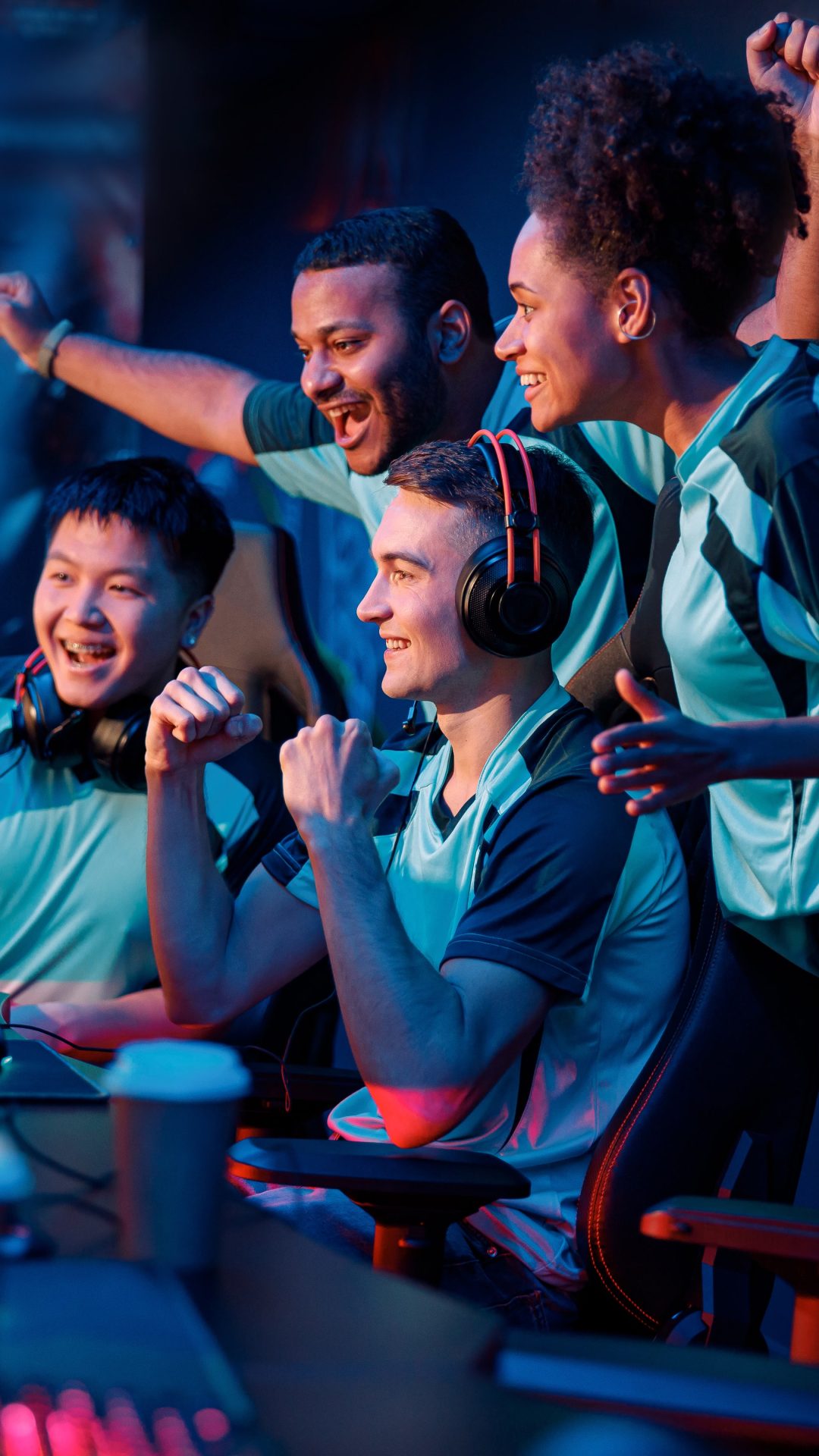 Multiracial cybersport gamers expressing success while raising hands up and smiling during participation in esports tournament in computer club